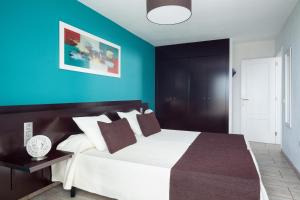 a bedroom with a large white bed with a blue wall at Aparthotel Los Dragos del Sur in Puerto de Santiago