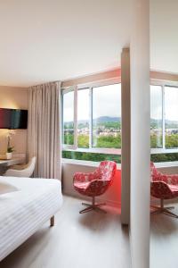una camera d'albergo con due sedie e un letto e finestre di Oceania Clermont Ferrand a Clermont-Ferrand