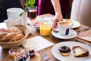 einen Tisch mit Frühstückslebensmitteln und eine Person mit einer Tasse Kaffee in der Unterkunft Hotel Zach in Innsbruck