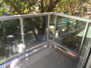 un balcón vacío con paredes de cristal y árboles en Apart Edificio Clever en La Plata