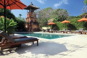 a pool with chairs and umbrellas next to a resort at The Pavilions Bali - CHSE Certified in Sanur