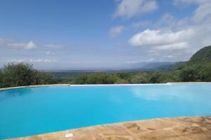 a large blue swimming pool with mountains in the background at Migombani Camp in Mto wa Mbu