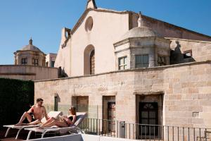 a group of people sitting on lounge chairs in front of a building at Hotel Palazzo Papaleo in Otranto
