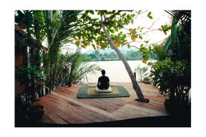 a person sitting on a yoga mat next to a body of water at Eden Eco Village in Kampot