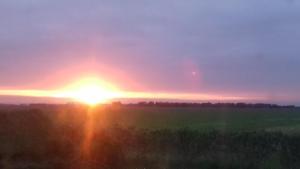 een zonsondergang boven een veld met de zon in de lucht bij Guesthouse Vestri-Gardsauki in Hvolsvöllur