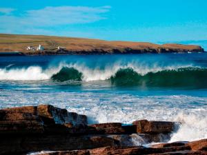 a large wave in the ocean with a house in the background at Norseman Hotel in Wick