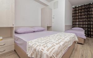 a white bedroom with two beds with purple sheets at Tea Two Apartman in Neum