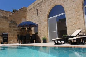 a pool with chairs and an umbrella next to a building at Simar in Qala