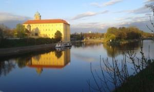 a building on a river with a boat in the water at Penzion Čokoláda in Poděbrady