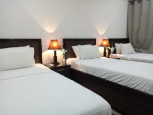 two beds in a hotel room with two lamps at Al-Fateh Hotel in Lahore