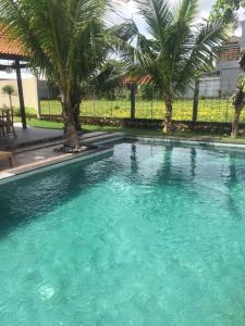 a swimming pool with blue water and palm trees at Cokelat Guest House in Tanah Lot