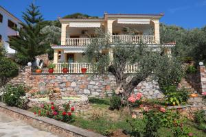 a house on a stone wall with a tree and flowers at Niki Apartments in Panormos Skopelos