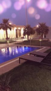 a swimming pool with benches and palm trees at night at Sofia Villa in Buraydah