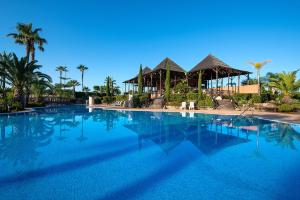 a large blue swimming pool with palm trees and huts at Puerto Antilla Grand Hotel in Islantilla