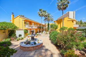 ein gelbes Haus mit einem Brunnen in der Mitte eines Gartens in der Unterkunft Hotel Cupidor in Paguera