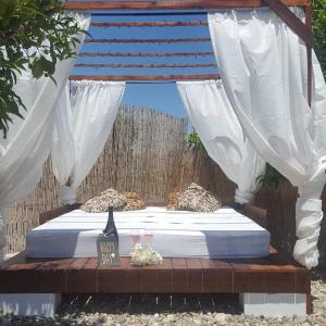 Una cama con cortinas blancas y dos vasos. en Finca Rayo del Sol, en Alhaurín el Grande