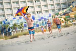 a young boy running on the beach with a kite at Crown Reef Beach Resort and Waterpark in Myrtle Beach