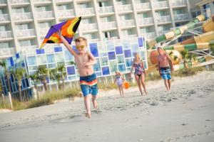 un jeune garçon en train de courir sur la plage avec un cerf-volant dans l'établissement Crown Reef Beach Resort and Waterpark, à Myrtle Beach