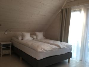 a bed with white sheets and pillows next to a window at Domki Szelega in Pobierowo