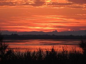 a sunset over the water with mountains in the background at Hotel Les Palmiers En Camargue in Saintes-Maries-de-la-Mer