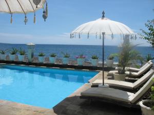 a swimming pool with an umbrella and the ocean at Kembali Beach Bungalows in Amed
