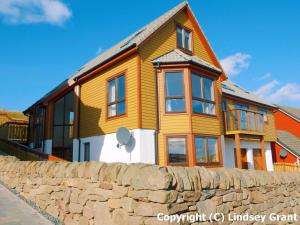 a large wooden house with a stone wall at Quoys Self Catering in Lerwick