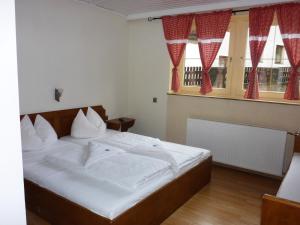 a bedroom with a bed with white sheets and red curtains at Sportpension Penhab in Saalbach-Hinterglemm