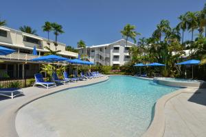 a swimming pool with chairs and blue umbrellas at Seascape Holidays at Beachfront Terraces in Port Douglas