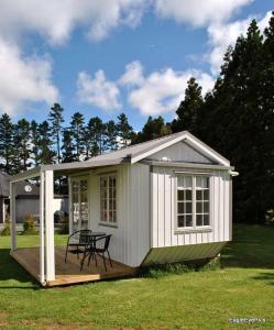 a small white shed with a table on a deck at Palm Drive 'Cozy Cabins' in Kerikeri