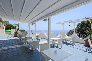 a patio with white tables and chairs and the ocean at Villa Guarracino Amalfi in Amalfi