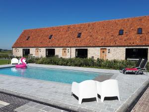 a swimming pool with white chairs and a house at vakantiehoeve 't Goed ter Leeuwen in De Haan