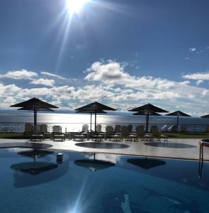 uma piscina com guarda-sóis e cadeiras e o oceano em Aegean Blue Studios em Afitos