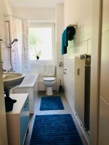 a bathroom with a sink and a toilet and blue rugs at KriDa Comfort Ferienwohnung in Garbsen