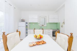 a white kitchen with a table with a bowl of fruit at Beach & park Apartment in Kaštela