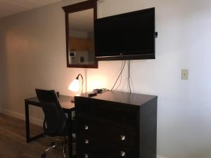 Habitación con escritorio y TV en la pared. en Belmont Inn & Suites Virginia Beach, en Virginia Beach