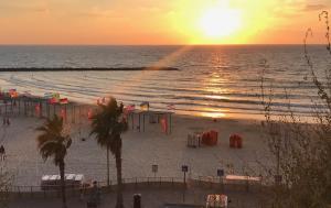 a beach with the sun setting over the ocean at Amazing apartment for 3 guests steps from the beach in Netanya