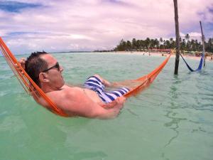 a man laying in a hammock in the water at Praia Hostel in Maragogi