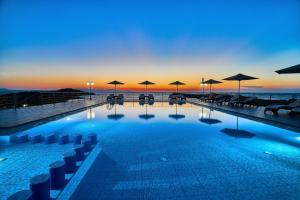 a swimming pool with umbrellas and the ocean at sunset at Nanakis Beach Apartments in Stavros