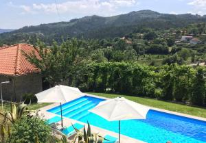una piscina con due ombrelloni di fronte a una casa di Casa Cima de Vila a Vieira do Minho