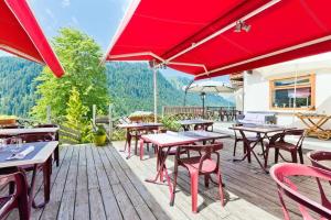 eine Terrasse mit Tischen, Stühlen und roten Sonnenschirmen in der Unterkunft Le Roitelet in Châtel