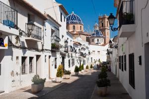 eine Gasse mit weißen Gebäuden und Topfpflanzen und einer Kirche in der Unterkunft Bungalow Altea junto al casco antiguo, piscina y barbacoa in Altea