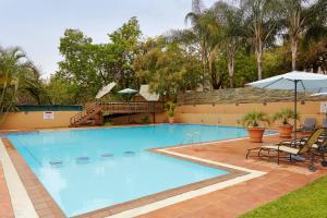 a large swimming pool with an umbrella and chairs at Waterberry Hill in Hazyview
