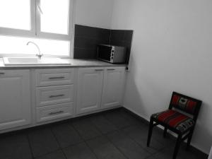 a kitchen with white cabinets and a microwave and a chair at Appartement quartier Dar Sebastian, Hammamet in Hammamet