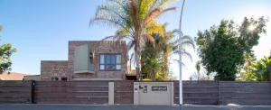 a house with a fence and palm trees at Earthbound Guest House in Oudtshoorn