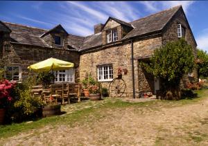 una antigua casa de piedra con sombrilla y mesas en Old Newham Farm, en Camelford