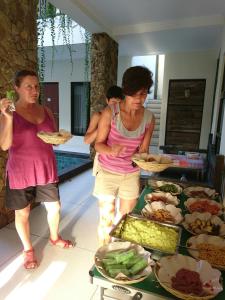 dwie kobiety stojące przed stołem z jedzeniem w obiekcie Umah Bagus w mieście Sanur