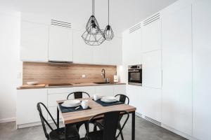 kuchnia z białymi szafkami oraz drewnianym stołem i krzesłami w obiekcie Unique 3City Apartments - Grey Apartment w Gdańsku