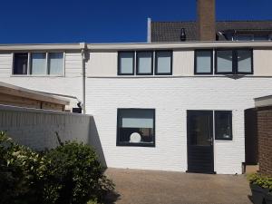 a white house with a black door and a window at Vakantiehuis Katwijk Andreasplein in Katwijk