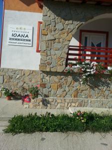 a building with a stone wall and a window with flowers at Pensiunea Agroturistica Ioana in Brăduleţ
