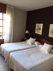 1 dormitorio con 2 camas con sábanas blancas y ventana en Hostal Santa Maria, en Cacabelos